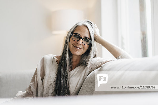 Porträt einer lächelnden Frau mit langen grauen Haaren auf der Couch sitzend