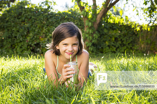 Portrait of little girl lying on a meadow drinking smoothie