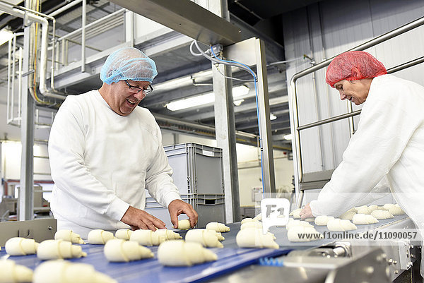 Arbeiter an der Produktionslinie einer Backfabrik mit Croissants