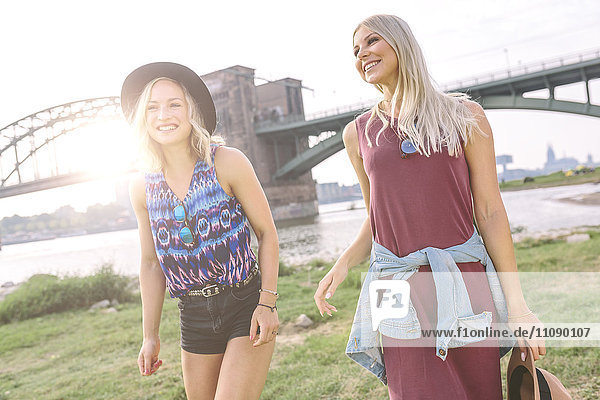 Zwei lächelnde junge Frauen  die am Flussufer spazieren gehen.