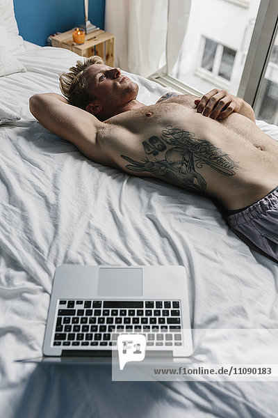 Schwuler Mann mit Tattoo auf dem Bett liegend