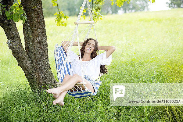 Glückliche Frau entspannt sich im Hängestuhl auf einer Wiese