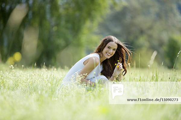 Happy woman crouching on a meadow picking flowers