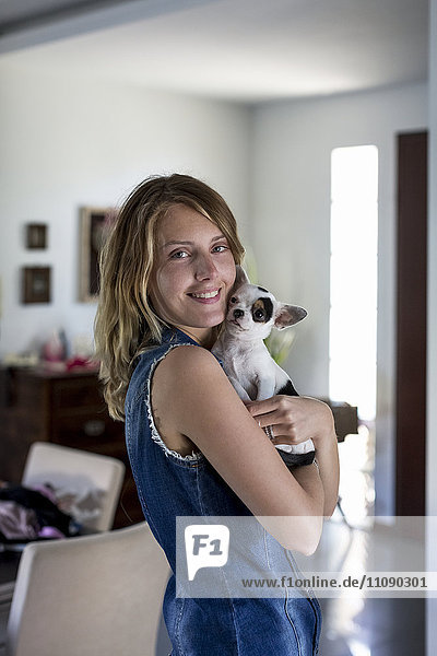 Lächelnde Frau mit Hund auf den Armen zu Hause
