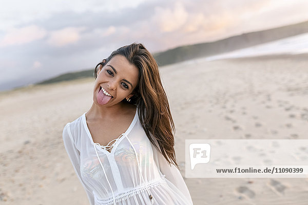 Portrait of young woman at beach  sticking out tongue