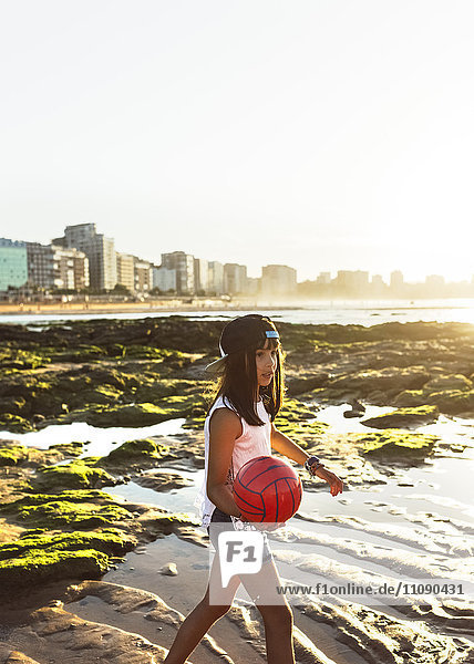 Mädchen spielt mit einem Ball am Strand bei Sonnenuntergang