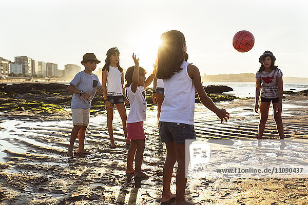 Kinder spielen mit einem Ball am Strand bei Sonnenuntergang