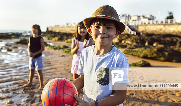 Portrait eines Jungen mit einem Ball am Strand bei Sonnenuntergang
