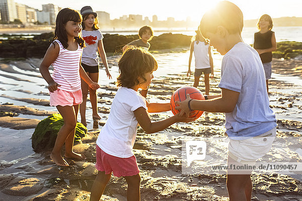 Kinder spielen mit einem Ball am Strand bei Sonnenuntergang