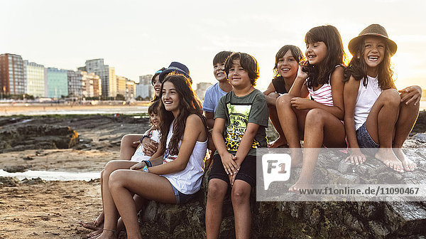Group of kids sitting on rock on the beach at sunset