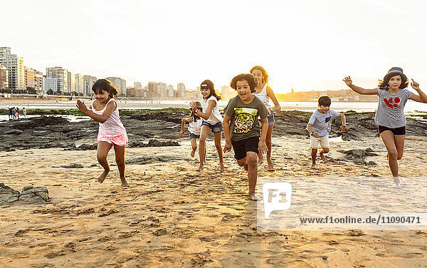 Kinder laufen bei Sonnenuntergang am Strand.