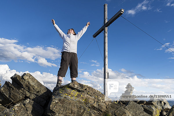 Junge Frau steht mit erhobenen Armen auf dem Berggipfel