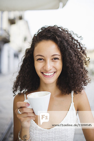 Porträt einer glücklichen jungen Frau beim Kaffeetrinken im Straßencafé