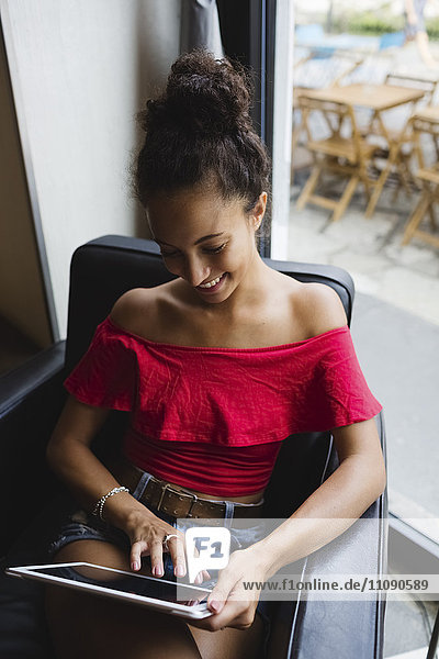 Lächelnde junge Frau sitzend in einem Café mit Tablette
