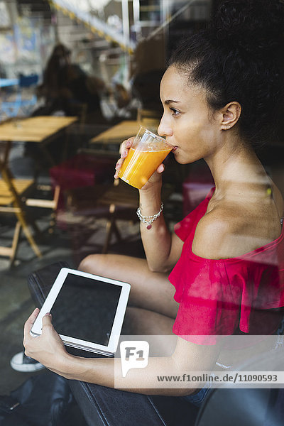 Junge Frau trinkt ein Glas Orangensaft in einem Coffee Shop