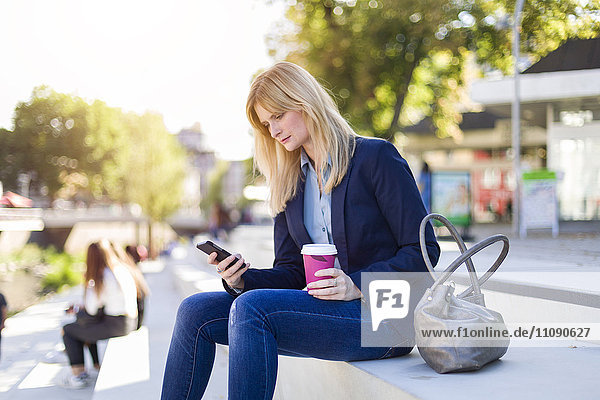 Blonde Geschäftsfrau mit Kaffee zum Anschauen von Smartphones