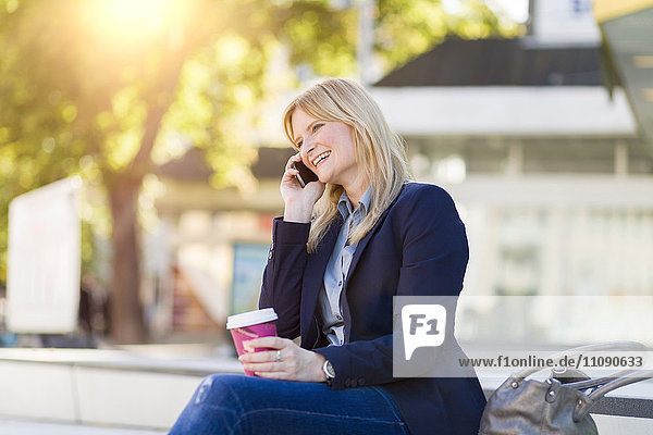 Lächelnde blonde Geschäftsfrau mit Kaffee zum Telefonieren
