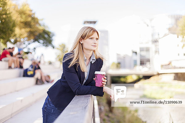 Geschäftsfrau mit Kaffee  die sich auf das Geländer lehnt und in die Ferne blickt