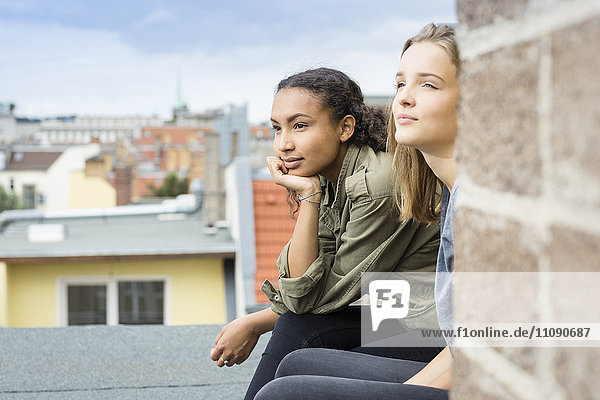 Zwei Teenager-Mädchen sitzen auf dem Dach und schauen in die Ferne.