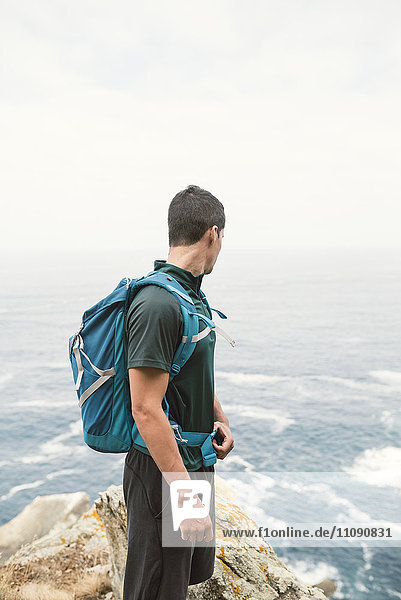 Junger Mann mit Rucksack vor dem Meer an der Küste