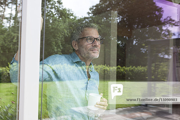 Mature man holding cup looking out of window
