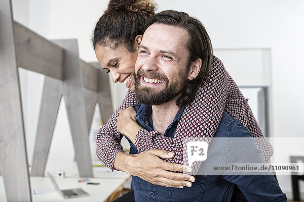 Man carrying happy woman piggyback in office