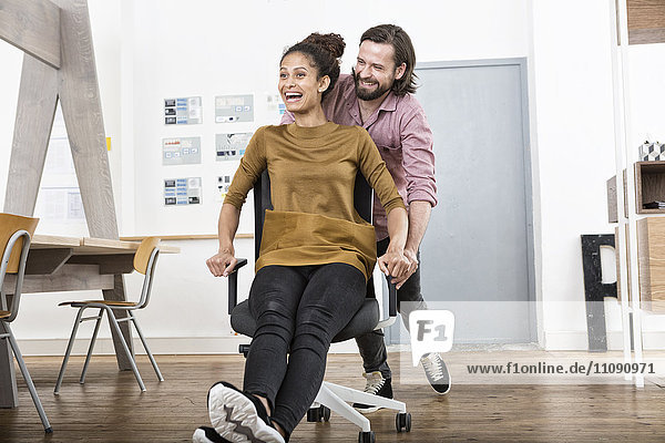 Mann schiebt glückliche Frau auf Bürostuhl