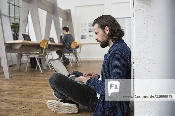 Man sitting on floor in office working on laptop