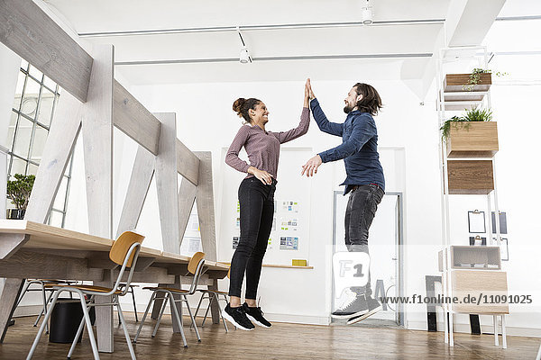 Zwei glückliche Kollegen im Büro Springen und High Fiving