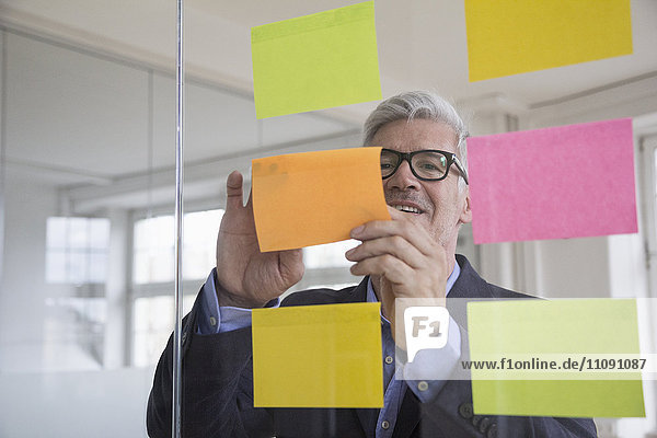 Businessman in office attaching adhesive notes at glass pane