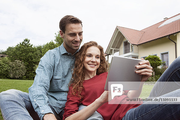 Smiling couple sitting in garden using tablet