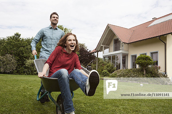 Man pushing happy woman in wheelbarrow in garden