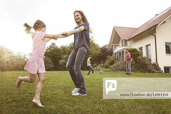 Mother and daughter dancing in garden with family in background