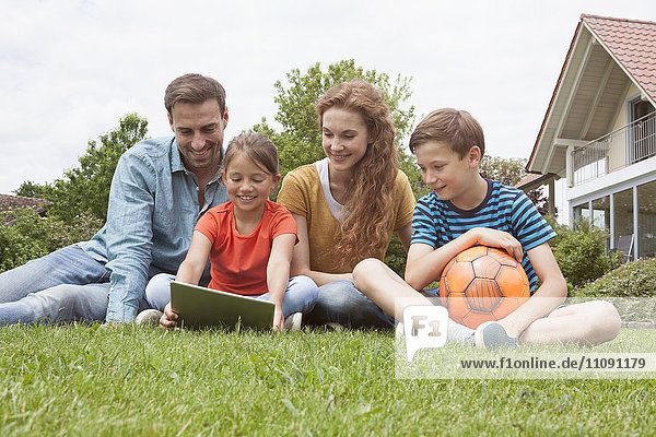 Smiling family sitting in garden with football using tablet