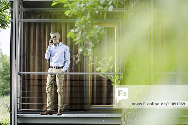 Mann am Telefon steht auf dem Balkon seines Hauses