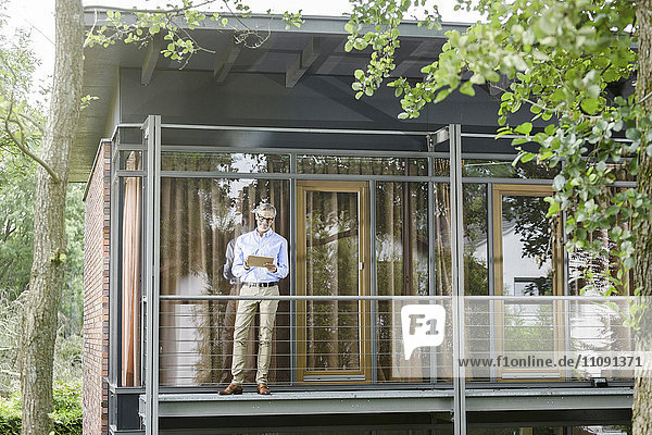 Mann steht auf dem Balkon seines Hauses mit Tablette