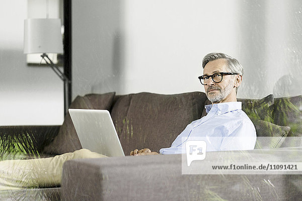Man sitting on couch in his living room with laptop
