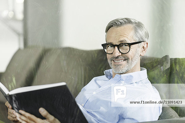 Porträt eines lächelnden Mannes auf der Couch mit Buch