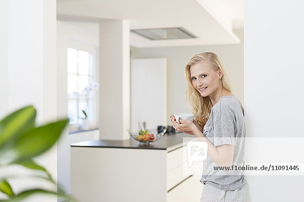 Lächelnde blonde Frau mit Tasse Kaffee in der Küche