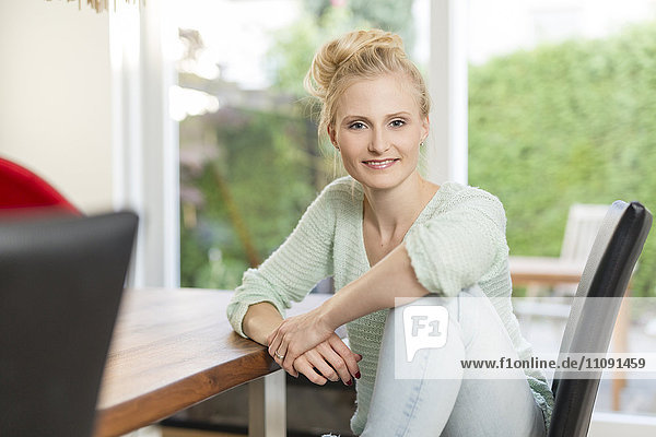 Porträt einer lächelnden blonden Frau  die am Esstisch sitzt
