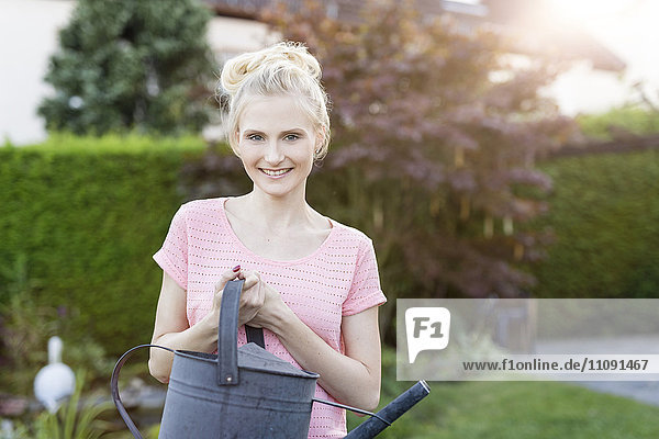 Portrait of blond woman holding watering can in garden