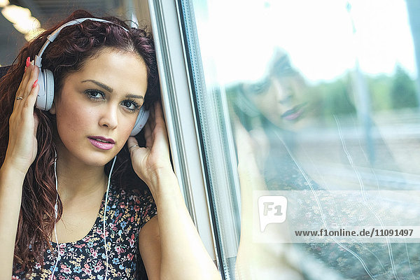 Porträt einer entspannten jungen Frau im Zug beim Musikhören mit Kopfhörern