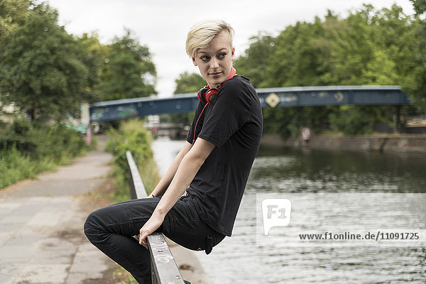 Junge Frau sitzt auf einem Geländer vor einem Kanal und beobachtet etwas.