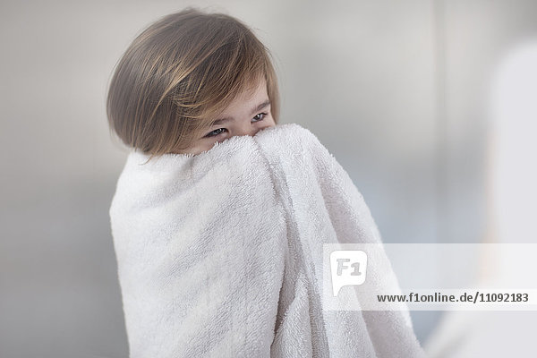 Kleines Mädchen in ein Handtuch gewickelt  das ihr Gesicht versteckt.