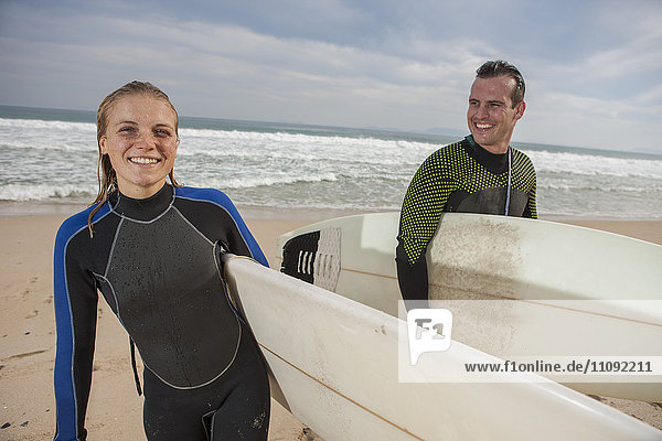 Lächelndes Paar mit Surfbrettern am Strand