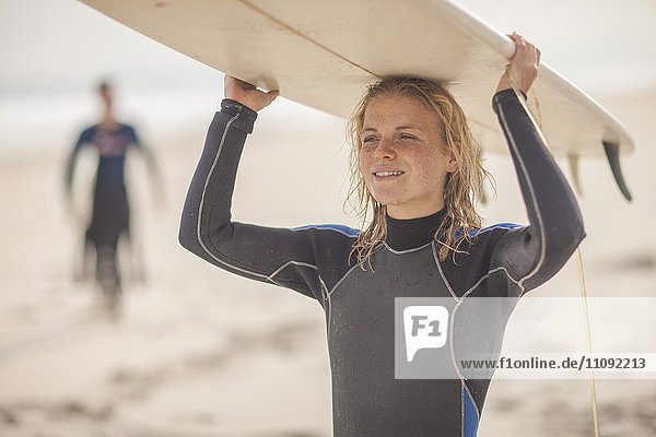 Junge Frau mit Surfbrett auf dem Kopf am Strand