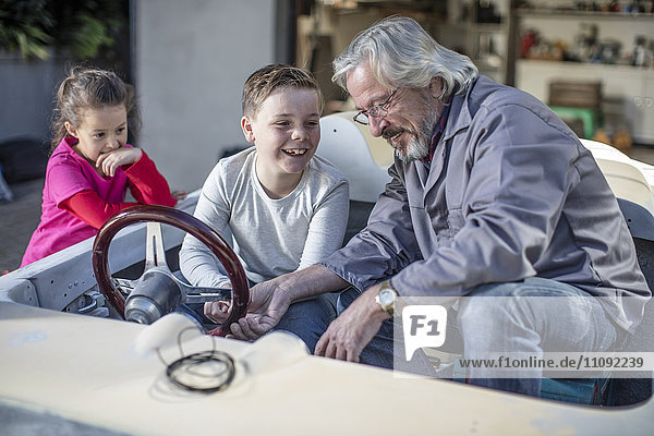 Lächelnder älterer Mann mit Junge und Mädchen in einem Cabriolet  das restauriert werden soll.