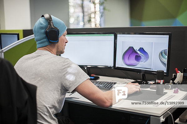 Junger Mann mit Kopfhörer bei der Arbeit am Computer im Büro