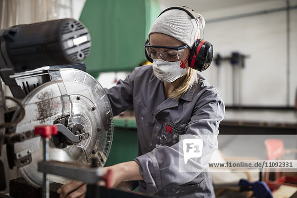 Woman wearing earmuffs and dust mask working on machine
