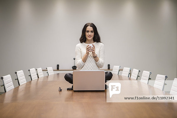Geschäftsfrau mit Laptop auf dem Konferenztisch sitzend  Tee trinkend